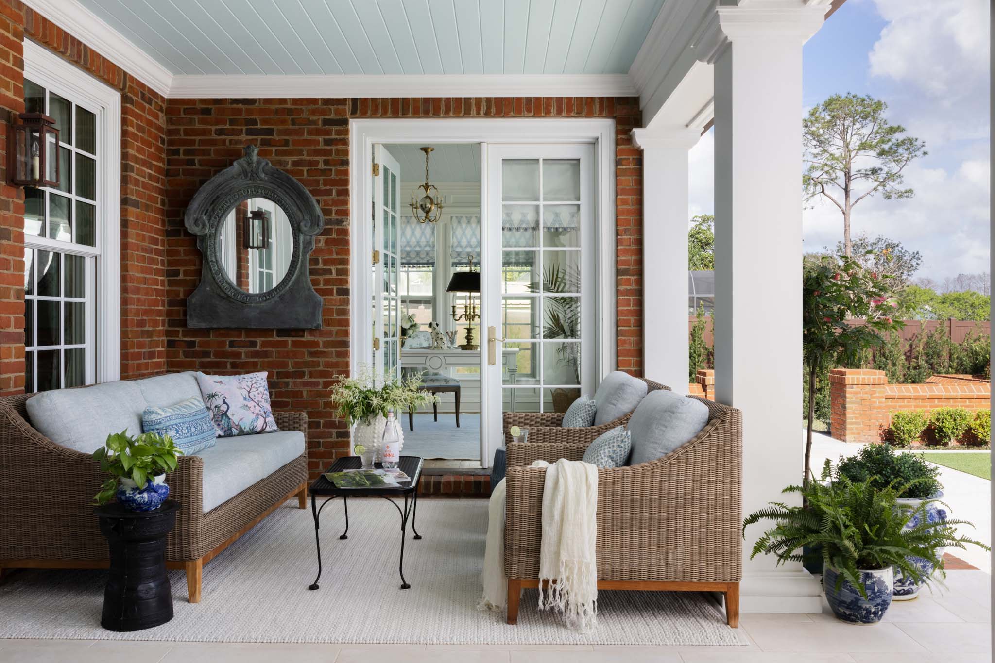 English country covered porch with wicker seating and blue tongue-and-groove ceiling